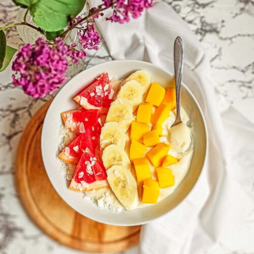 Bowl of rice porridge with fresh grapefruit, banana, mango and coconut flakes